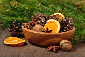 Different kinds of spices, nuts, dried oranges and cones in bowl