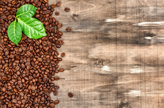 Brown coffee beans green leaves wooden background