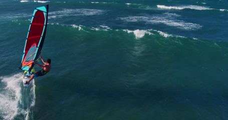Aerial view of windsurfer gliding across blue ocean jumping off wave, extreme sport