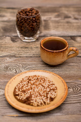 Small cup of coffee, glass with roasted coffee beans, cookies with sesame seedson wooden background