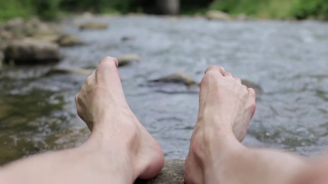 Bare feet man sitting on the beach of a mountain river