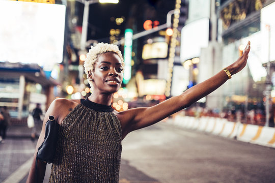 USA, New York City, young woman hailing a taxi on Times Square at night