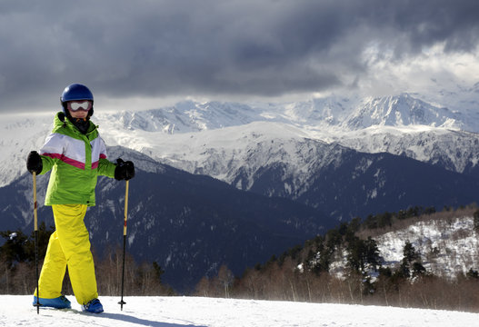 Young skier with ski poles in sun mountains and cloudy gray sky