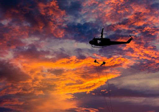    silhouette soldiers in action rappelling climb down from helicopter with military mission counter terrorism assault training on sunset background 