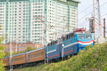 Train with multicolored locomotive and orange wagons moves on bank against skyline background. Moscow, Russia. 
