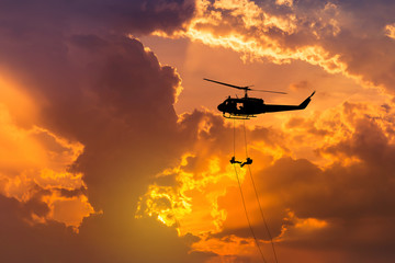    silhouette soldiers in action rappelling climb down from helicopter with military mission...