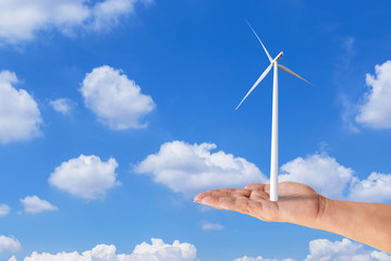 woman hand holding green tree with wind turbines generating electricity on blue sky background.Ecology concept.   
