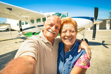 Senior happy couple taking selfie with ultralight plane for tour around the world - Active elderly concept with retired people enjoying pension moments - Bright and warm sunny afternoon color tones