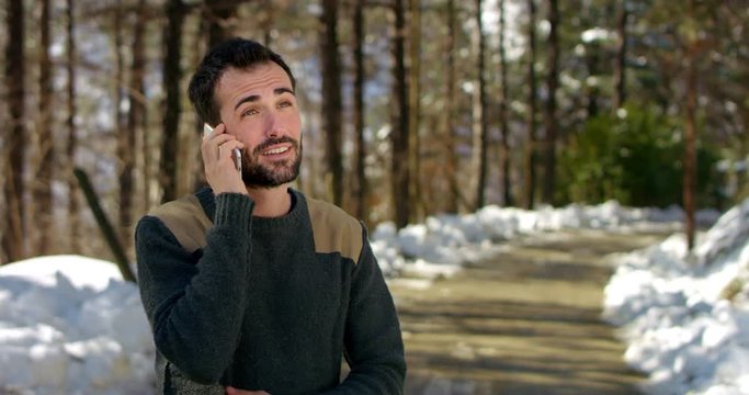 young beautiful and elegant man filmed while phoning with a smart phone happily with friends or someone in a pleasant natural environment , more precisely in a forest at the foot of a mountain