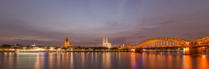 Fototapeta na wymiar Illuminated Cologne Cathedral and bridge at night in Cologne, panoramic view