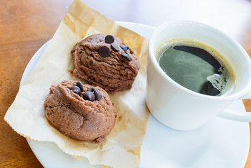 Black coffee cup with chocolate cookie on wooden background