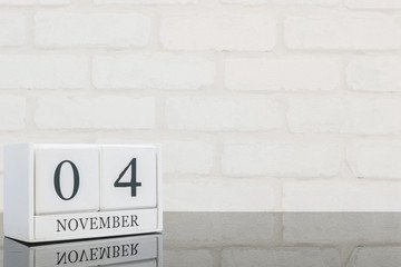 Closeup white wooden calendar with black 4 november word on black glass table and white brick wall textured background with copy space , selective focus at the calendar