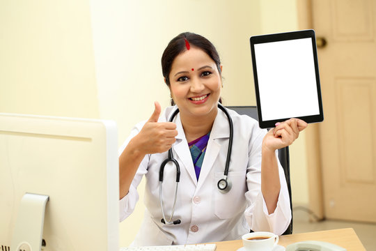 Traditional female doctor holding tablet computer at clinic desk
