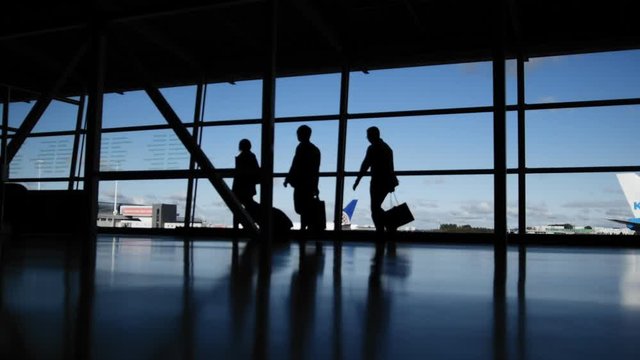 Travellers with suitcases and baggage in airport walking to departures in front of window, silhouette