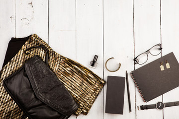 set of woman stuff on white wooden desk: dress, bag, watch, glasses, notepad, accessories