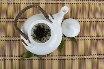 White teapot with dry black tea leaves