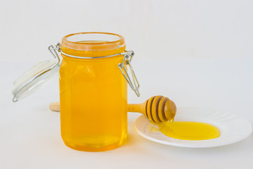 Jar with honey and Нoney dipper on white saucer
