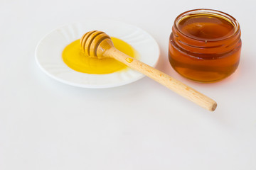 Jar with a dark honey. Honey dipper  on a white saucer with a li