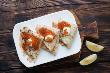 Crepes with sour cream and red caviar in a rustic wooden setting