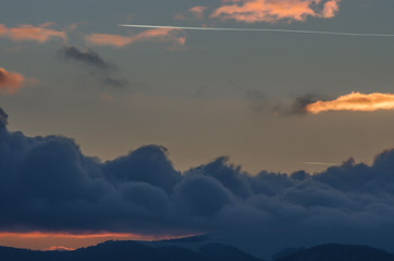 Jet plane flying in the mountains above the clouds at sunset.