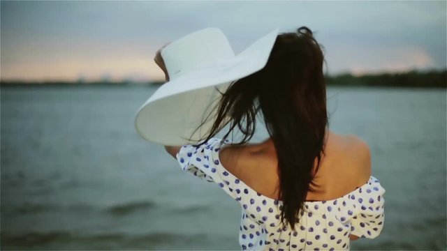 A middle aged woman putting off her hat on the beach at sunset.