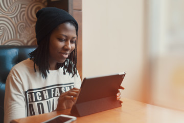 Beautiful black girl smiling and working on tablet in cafe