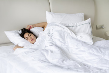 young woman happily sleeping in white bed