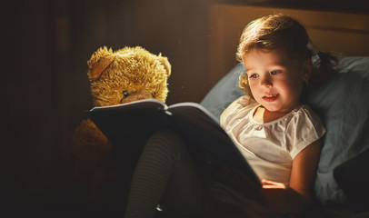 child girl reading a book in bed