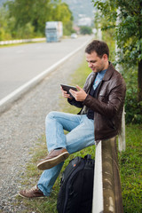 Obraz premium Man sitting on a road fence with gps tablet pc and using online maps
