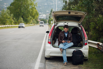 Fototapeta na wymiar leisure, road trip, travel and people concept - happy man searching location using tablet with online map sitting on trunk of hatchback car outdoors