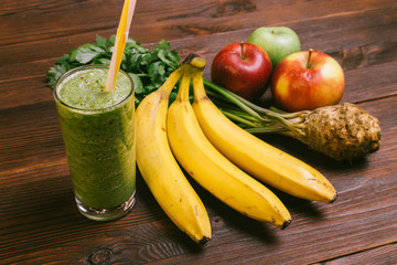 Glass of green smoothie with yellow straw on a wooden table next