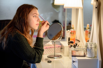 junge Frau beim Schminken vor Spiegel