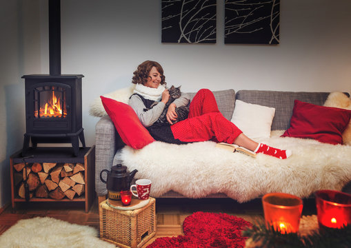 woman hugging cat lying on a cosy sofa beside fireplace