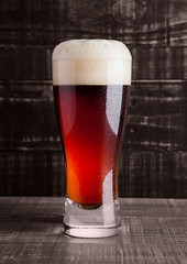 Glass of brown ale beer with foam on wood