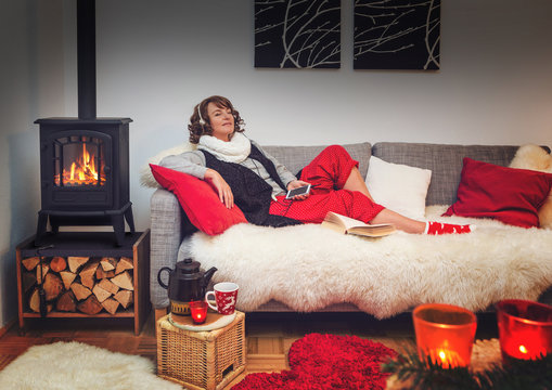 woman on a cosy sofa beside fireplace listening to music