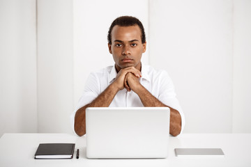Young successful african businessman sitting at workplace with laptop.