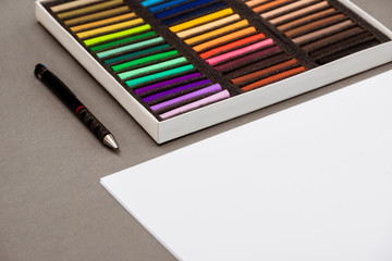 Naklejka premium Colorful pastel, pen, paper on grey table.