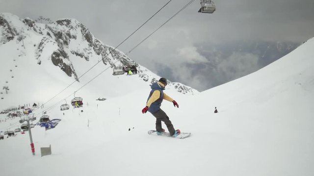 Snowboarder ride down on slope at snowy mountains. Uniform. Ski lifts. Ski resort. Extreme hobby. Slow motion