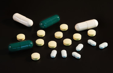 White and green capsules and tablets on black background
