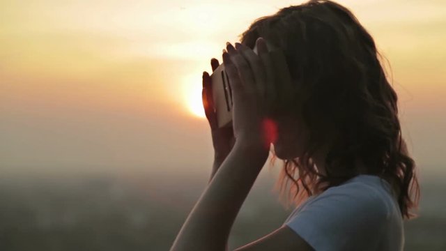 Woman uses a virtual reality glasses. Sunset light, sun lens flares, golden hour. Relax, nature and technology concept