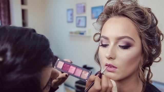 Make up artist doing professional makeup of young woman in beauty studio