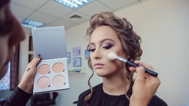 Make up artist doing professional makeup of young woman in beauty studio