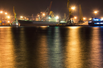 Fototapeta na wymiar Cargo vessel is moored at container terminal of port Odessa, Ukraine. Crane lights are on background. Night view picture