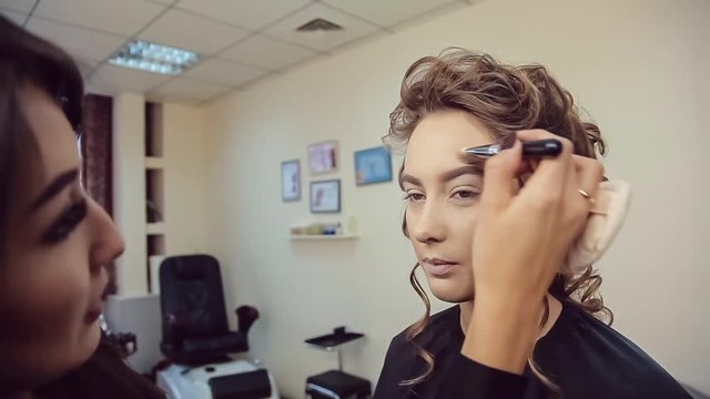 Make up artist doing professional makeup of young woman in beauty studio