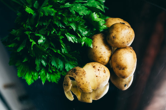 A bunch of parsley and raw unpeeled potatoes are on a black background and reflects in the mirror.