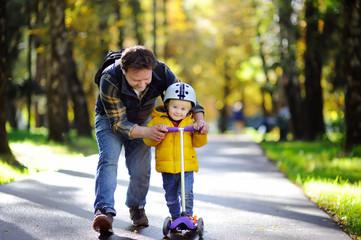 Father showing his toddler son how to ride a scooter