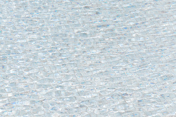 Pool water with waves and reflections of the floor tiles on water. Texture of tiles and sun reflection on the pool water.