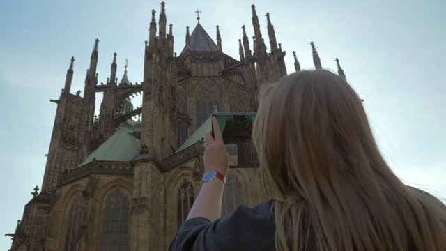 Low angle shot of woman looking at St. Vitus Cathedral and taking picture on smart phone. Landmarks of Prague, Czech Republic