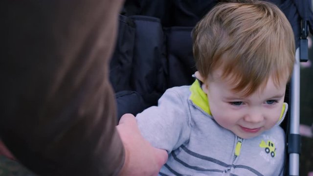 Adorable baby boy being buckled into a stroller in a park
