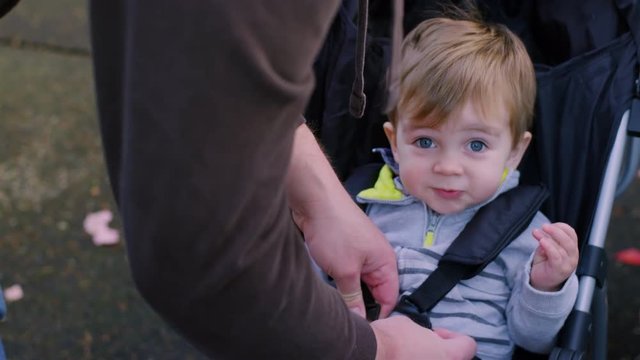 Adorable baby boy being buckled into a stroller in a park